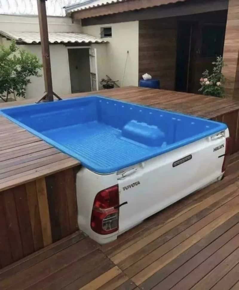 A pickup truck bed converted into a swimming pool on a wooden deck.