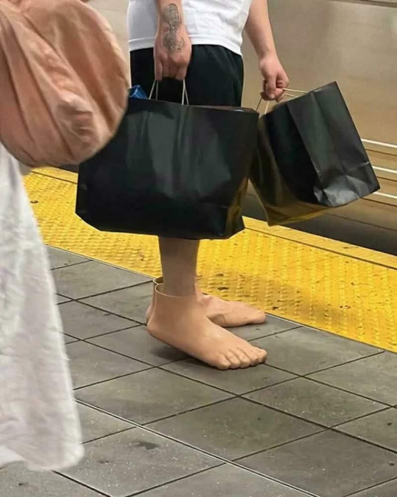 Person with feet in slippers holding shopping bags at a station.