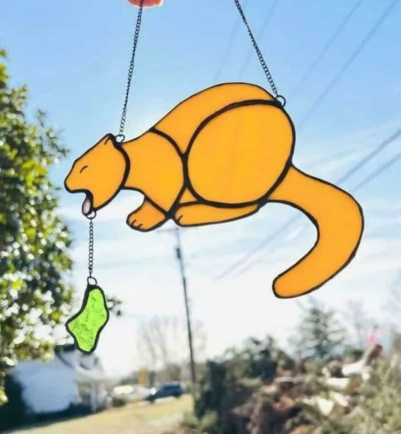 Suncatcher of a cat with a green fish toy hanging from its mouth.