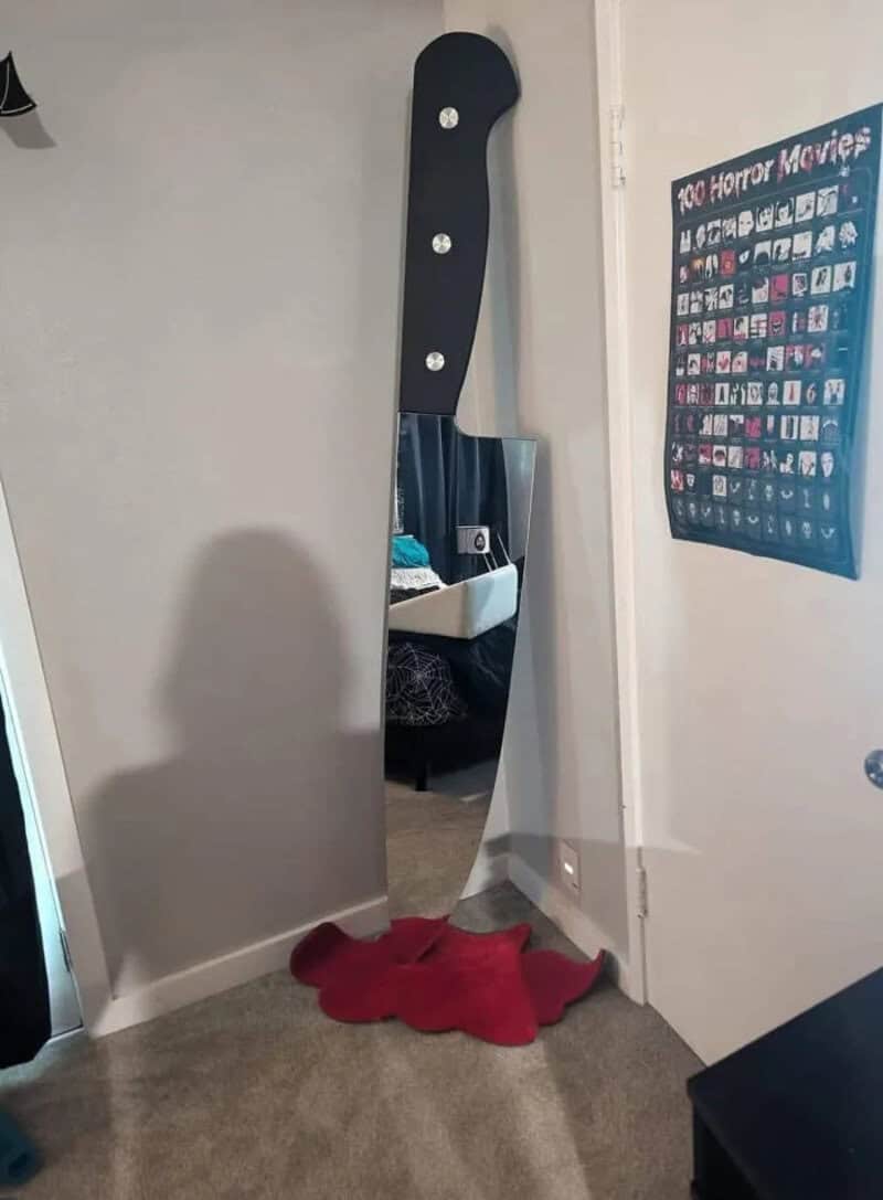 Full-length mirror with a black handle and a red rug in front, in a room.