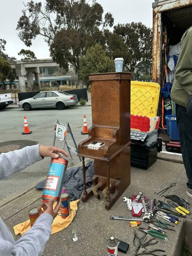 Old upright piano with tools and supplies around it, outdoors near a truck.