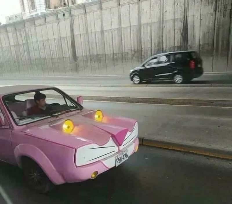 Pink car with cat face design, yellow eyes, and ears, on a city street.