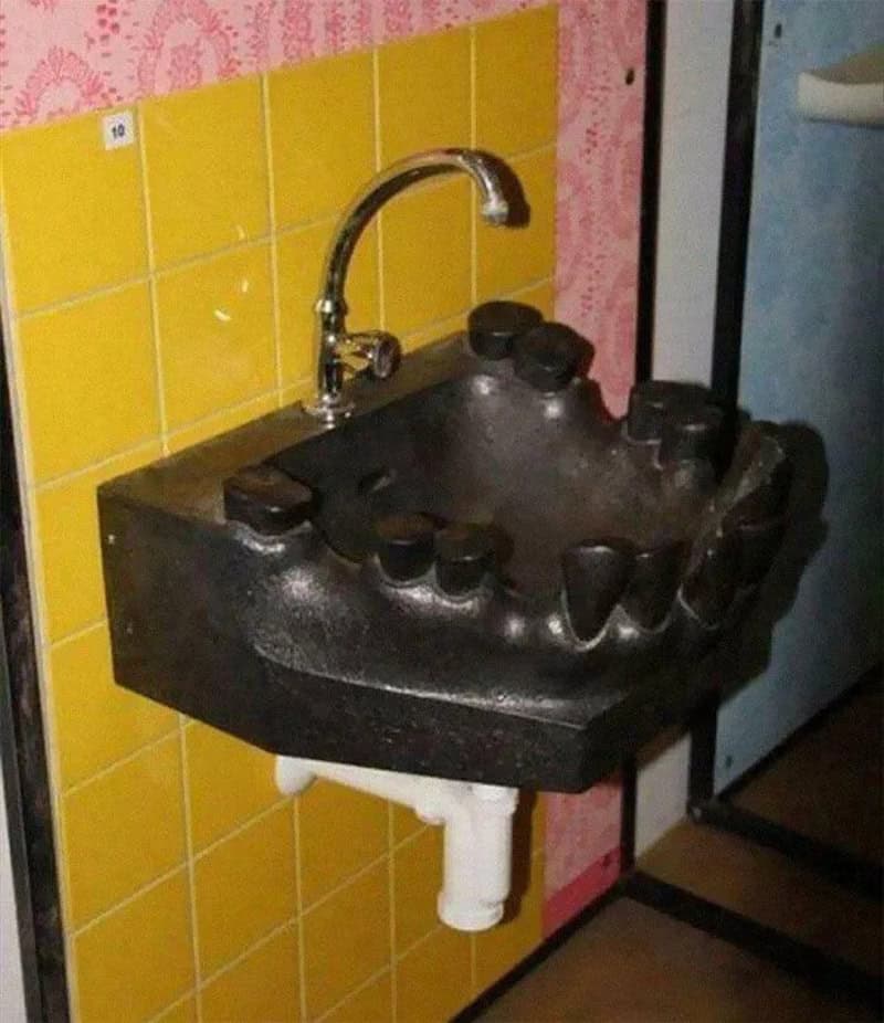 Black sink with large teeth design and faucet, yellow tiled wall background.