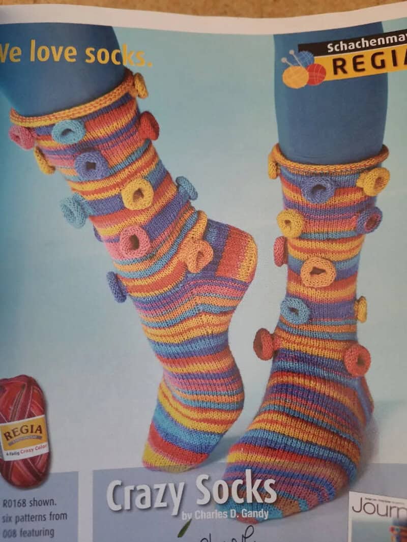 Colorful knitted socks with circular patterns, worn on legs with blue pants.