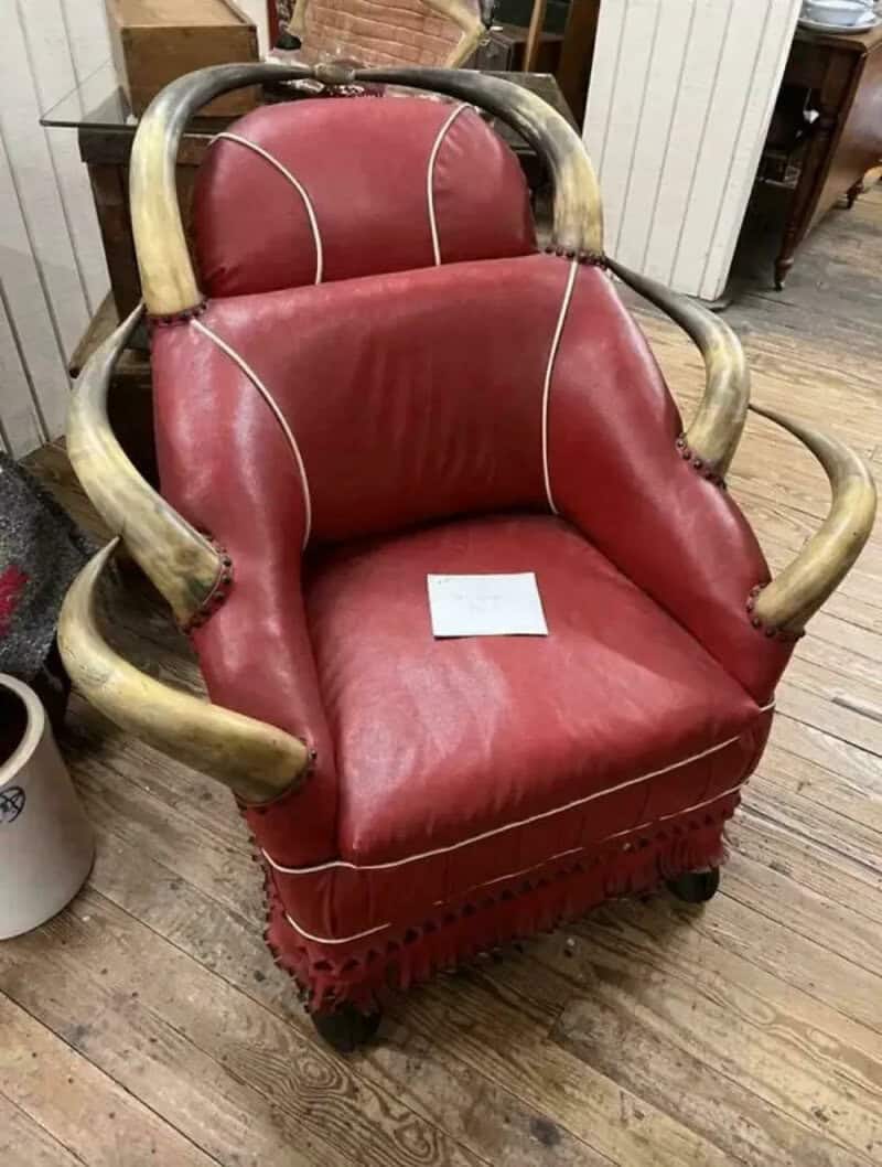 Vintage red armchair with wooden armrests and a fringed bottom, on a wooden floor.