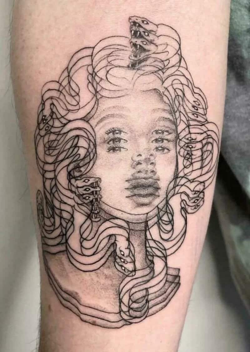 Tattoo of a woman's face with flowing hair and snakes, in black ink.
