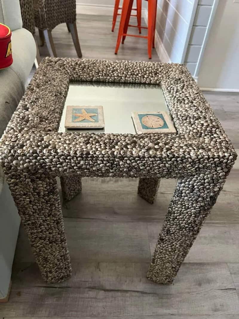 Coastal-themed side table with a glass top, decorated with seashells and starfish.