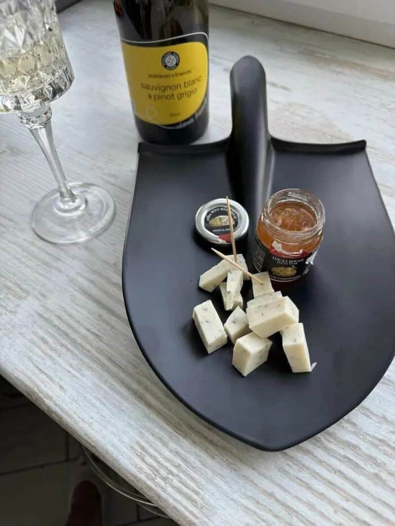 Cheese cubes, jam, wine, and a glass on a black tray on a white table.