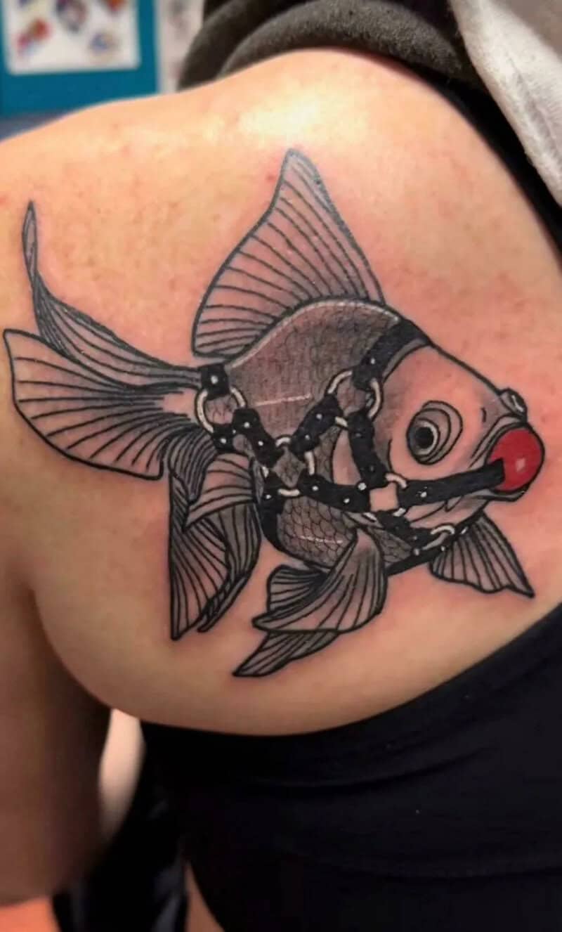 Tattoo of a fish with a harness and a red nose on skin.