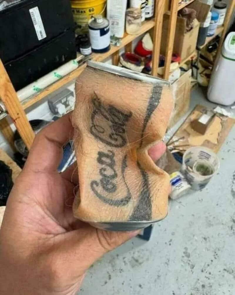 Crushed soda can with Coca-Cola logo, held in hand in a workshop.