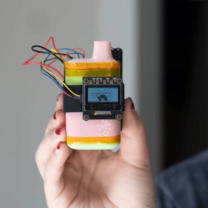 Hand holding a small robot with wires and a screen displaying a bug icon.