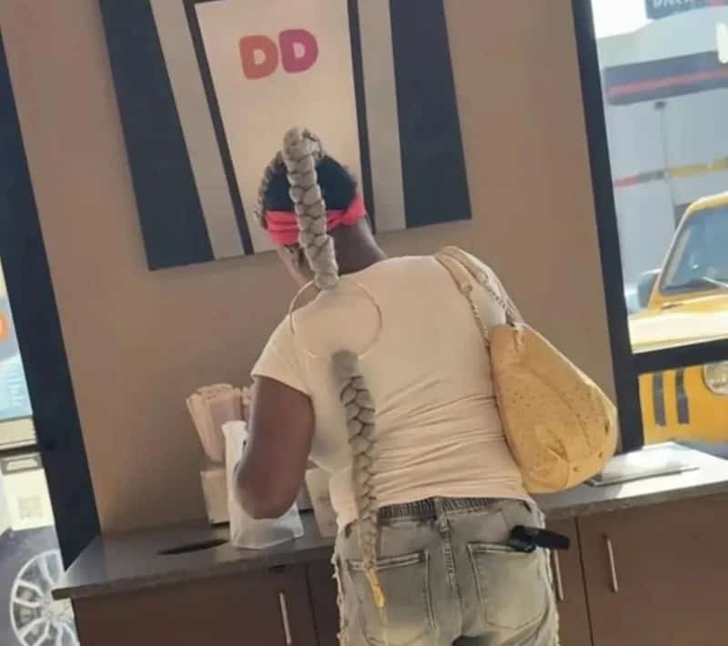 Person with long braided hair wearing a white shirt and jeans at a counter.