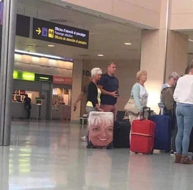 Luggage with a large printed face of a smiling woman on it at an airport.