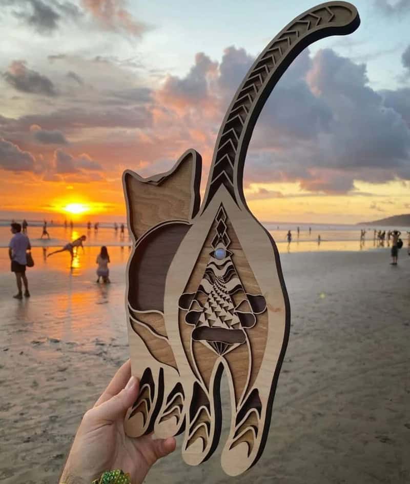 Wooden cat-shaped sculpture with intricate cutouts held at the beach during sunset.
