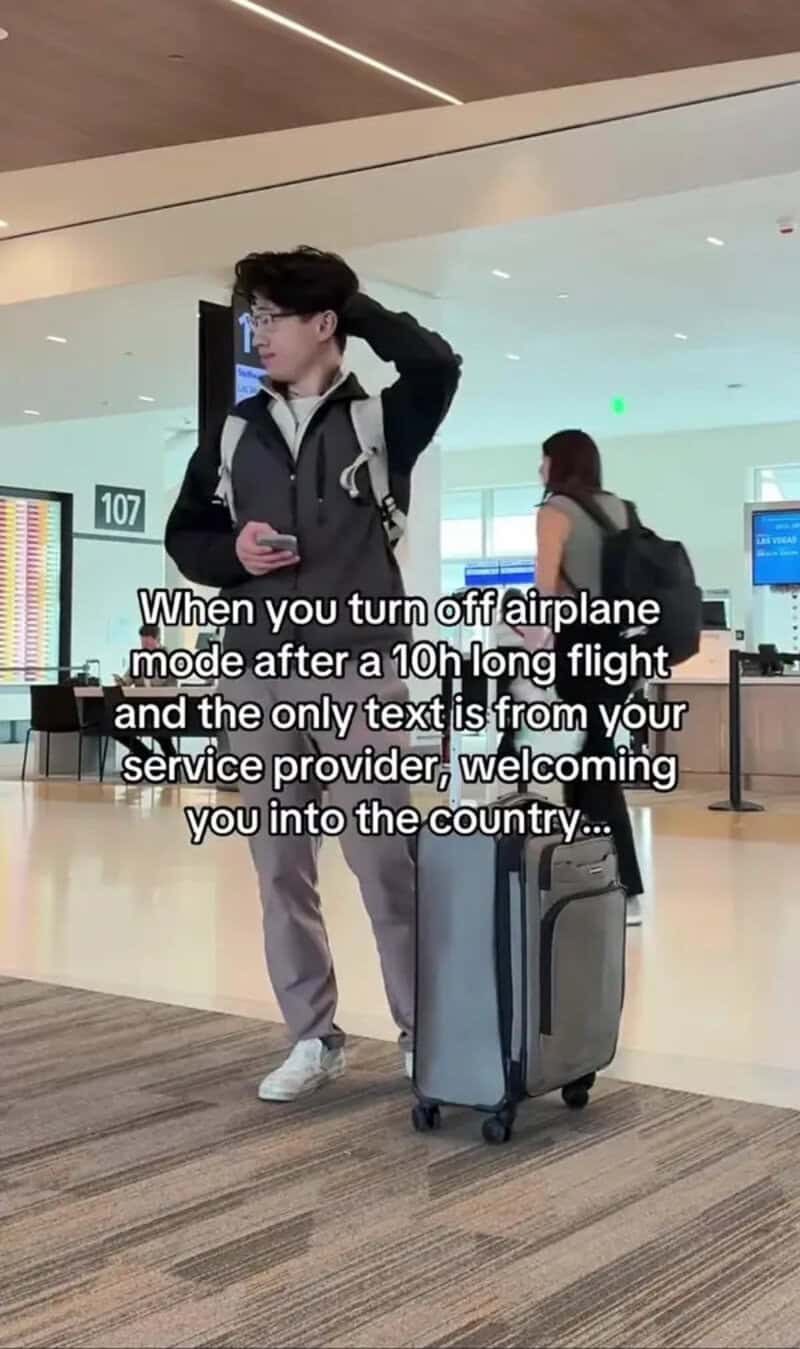 Young man at airport with luggage, looking at phone, after turning off airplane mode.