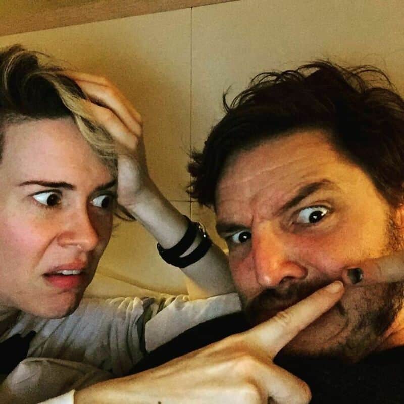 Two people making surprised faces, one with hand on head, the other with finger on lips.