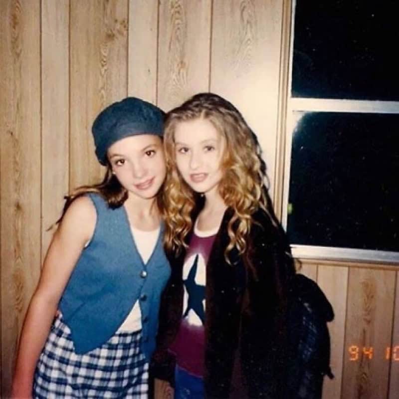 Two young girls with curly hair posing together in a wooden room.