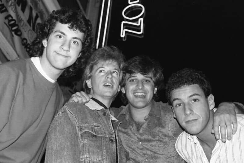 Four young men smiling, with one wearing a striped shirt, in a black and white photo.
