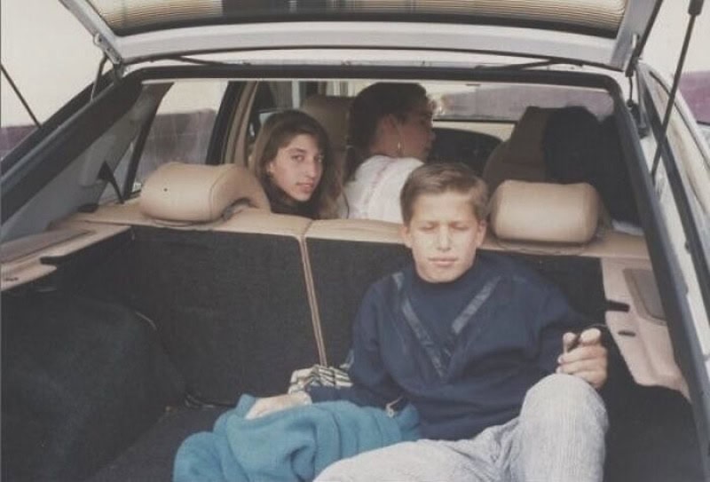 Four young people sitting in the back of a car, two girls and two boys, with one boy looking at his,.