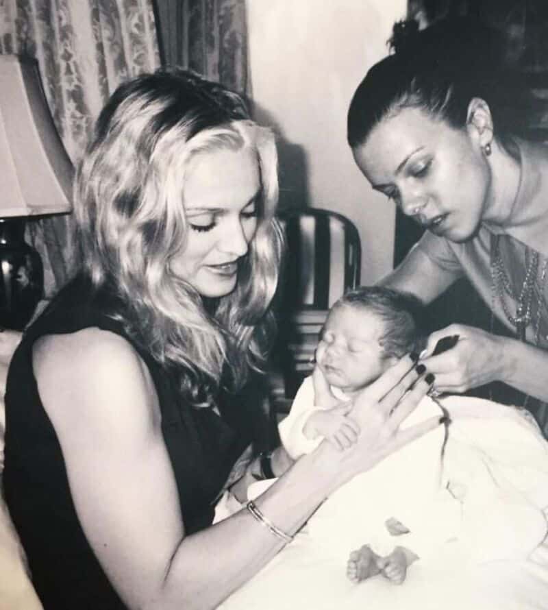 Two women holding a newborn baby, one woman with blonde hair and the other with dark hair.