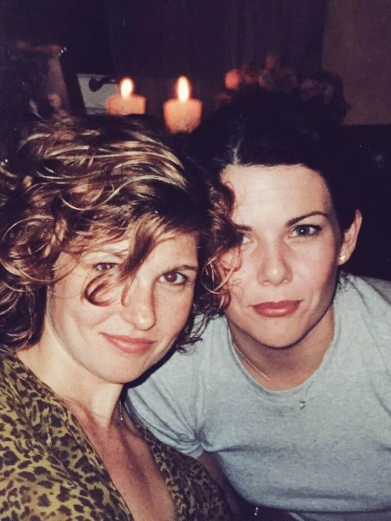 Two women with short hair smiling, candles in the background.
