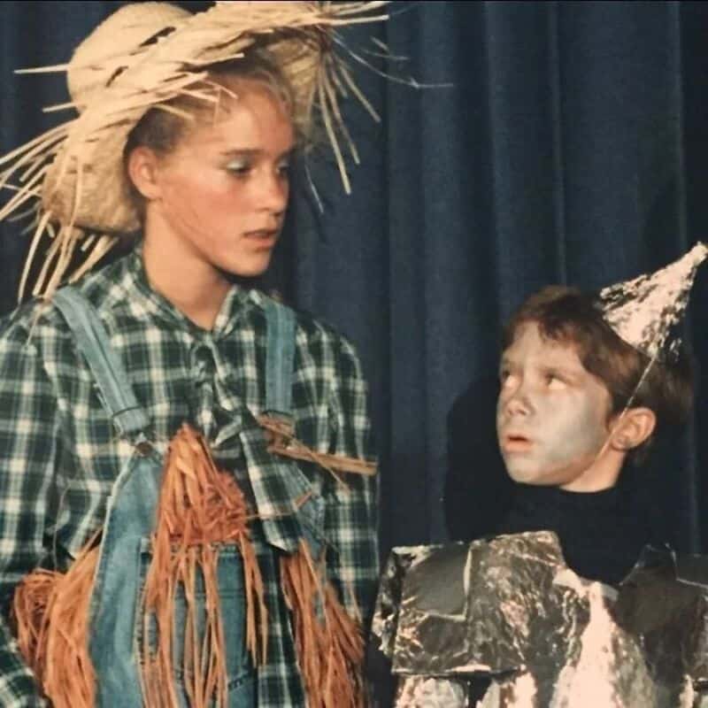 Two children in costumes, one with a straw hat and plaid shirt, the other with a painted face and a.