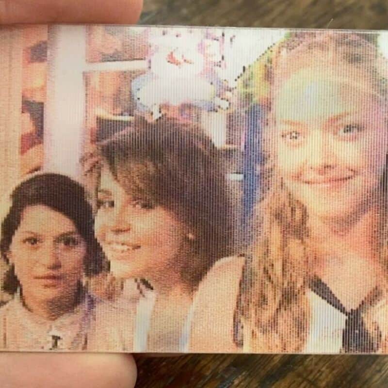 Three young women smiling, with a blurred background of a room.