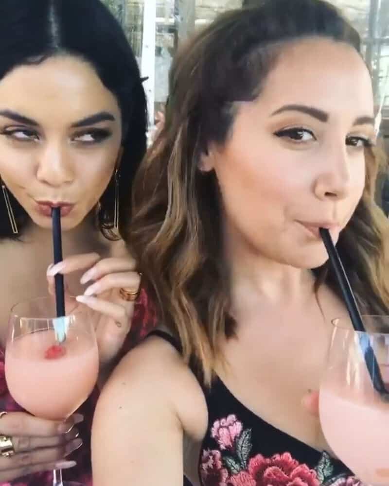 Two women drinking pink beverages with straws, smiling and looking at the camera.