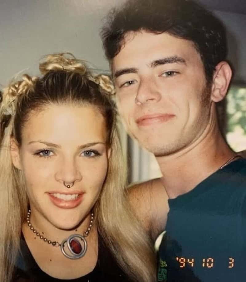 Young woman with blonde hair and septum piercing, young man with dark hair, smiling together.