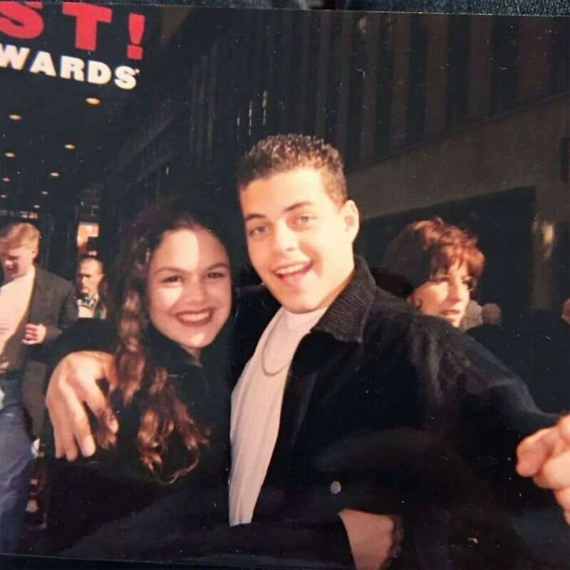 Two young people smiling and hugging at an event, with a crowd in the background.