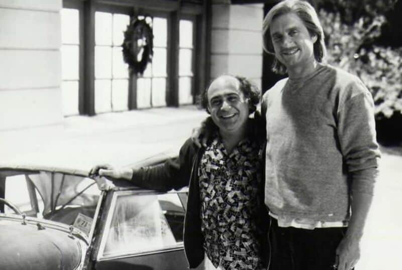 Two men smiling, one with glasses, standing next to a vintage car.