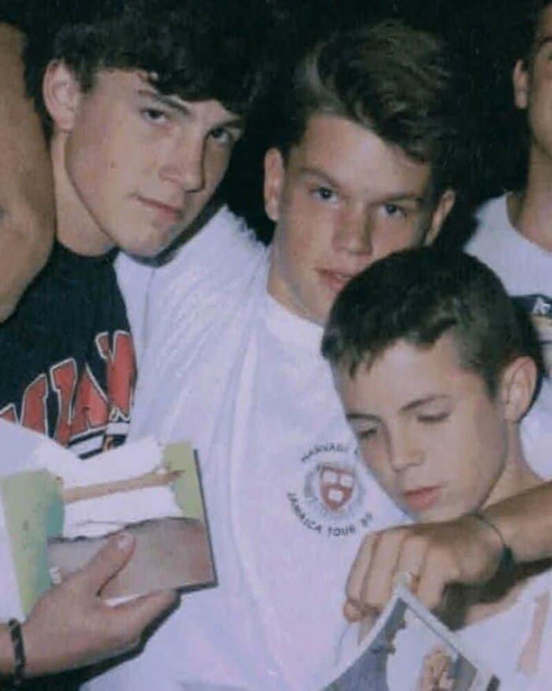Three young boys with short hair, one holding a photo, in a casual setting.