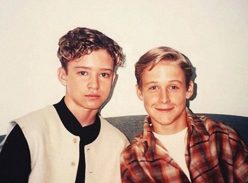 Two young boys with curly and straight hair, one in a varsity jacket, sitting on a couch.