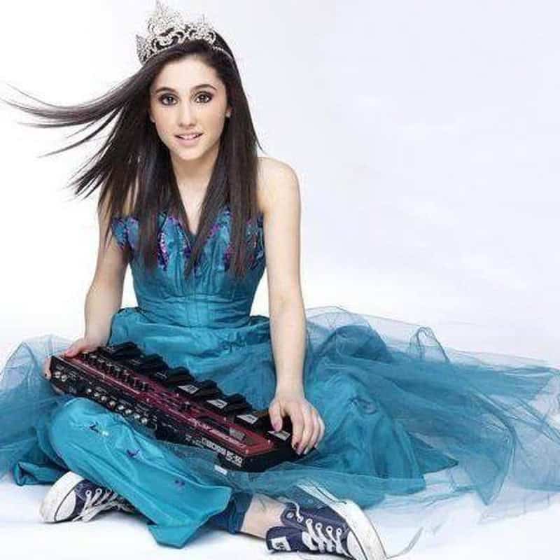 Young girl in a blue dress with a tiara, sitting with a keyboard, smiling.