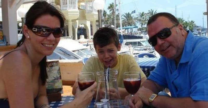 Family enjoying drinks at a marina with boats and palm trees in the background.