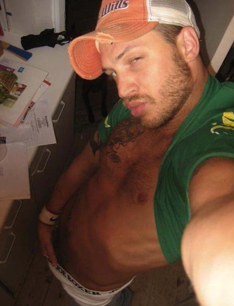 Man taking a selfie, wearing a cap and green shirt, showing his abs.