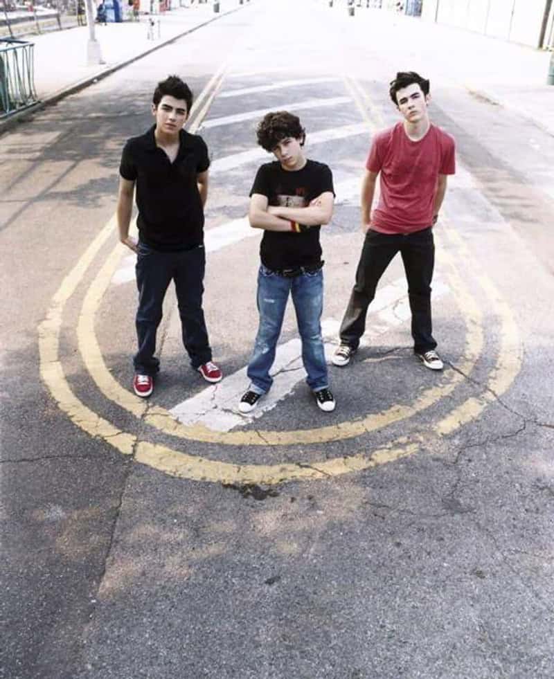 Three young men standing on a street with a yellow circle painted on the ground.