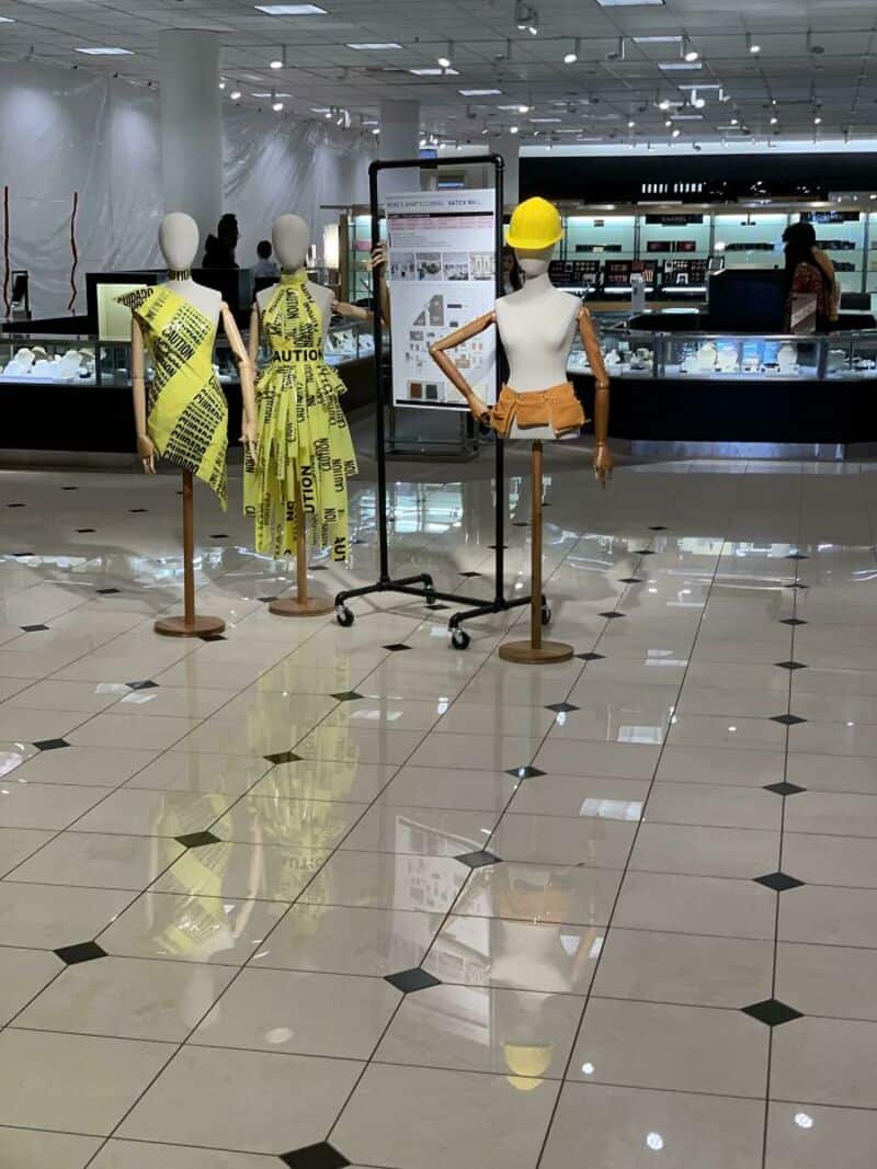 Mannequins with caution tape and safety gear display in a shopping mall.