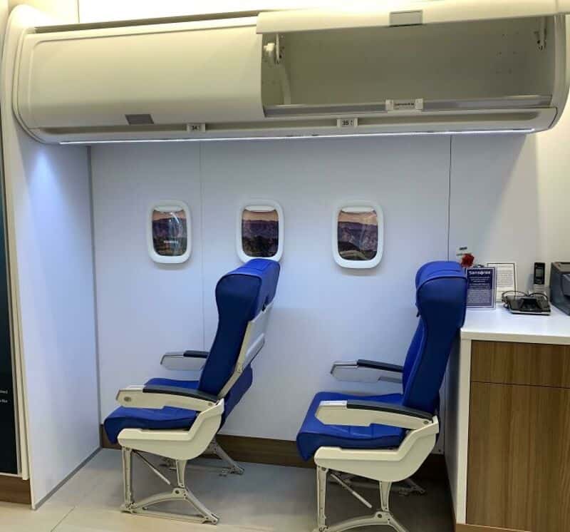 Empty airplane seats with blue upholstery and windows behind, near a small counter.