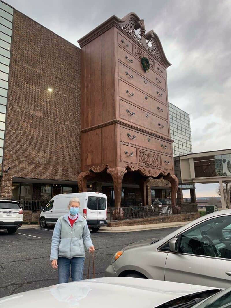 Giant antique dresser in a parking lot with cars and a person wearing a mask.