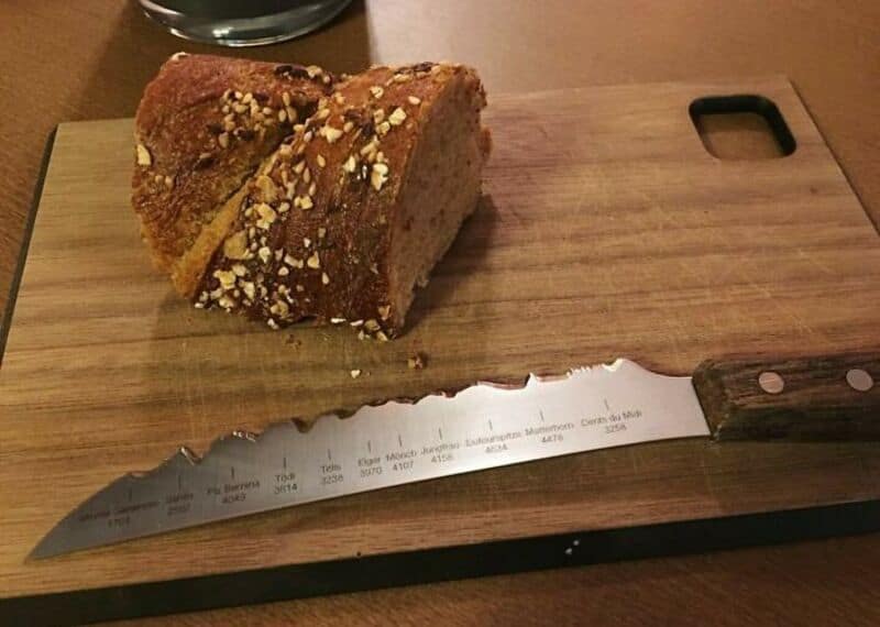 A loaf of bread on a wooden cutting board with a serrated knife.