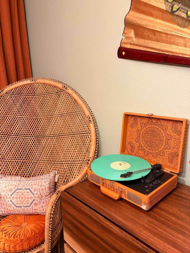 Vintage record player on a wooden table with a wicker chair nearby.