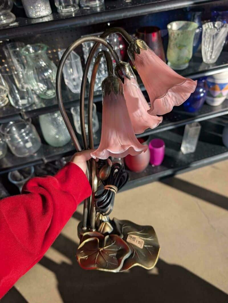 Hand holding a vintage floral lamp with three pink flower-shaped lampshades at thrift store.