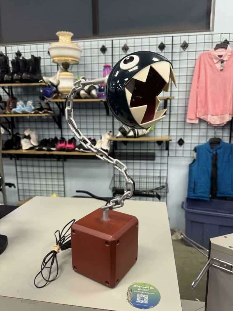 Pac-Man inspired lamp with a black spherical head and sharp teeth, on a chain arm.