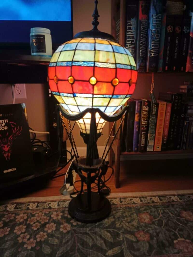 Colorful stained glass lamp with a black base and chain, on a wooden floor near a bookshelf.