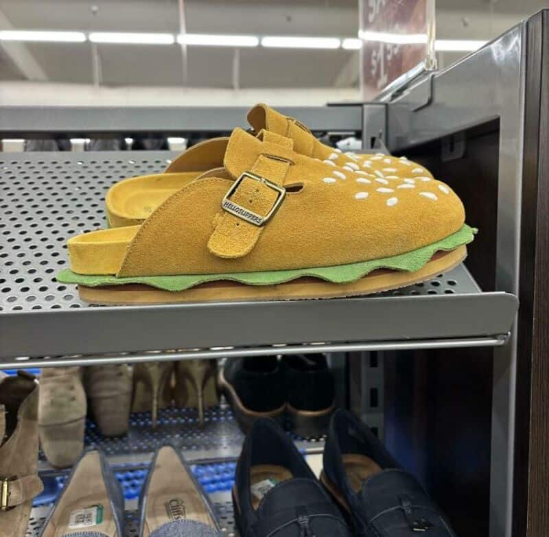 Yellow slippers shaped like a mustard bottle with white dots and green sole, on store shelf.