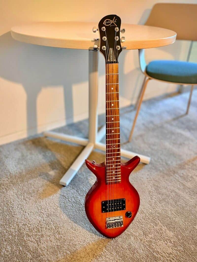 Red electric guitar leaning against a table in a room.