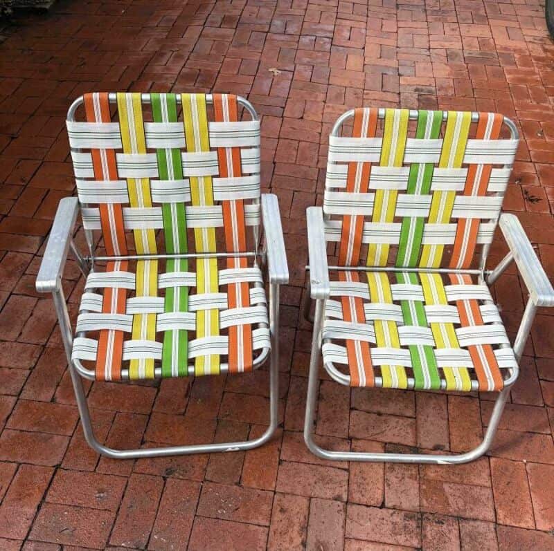 Two colorful woven patio chairs on a brick patio.