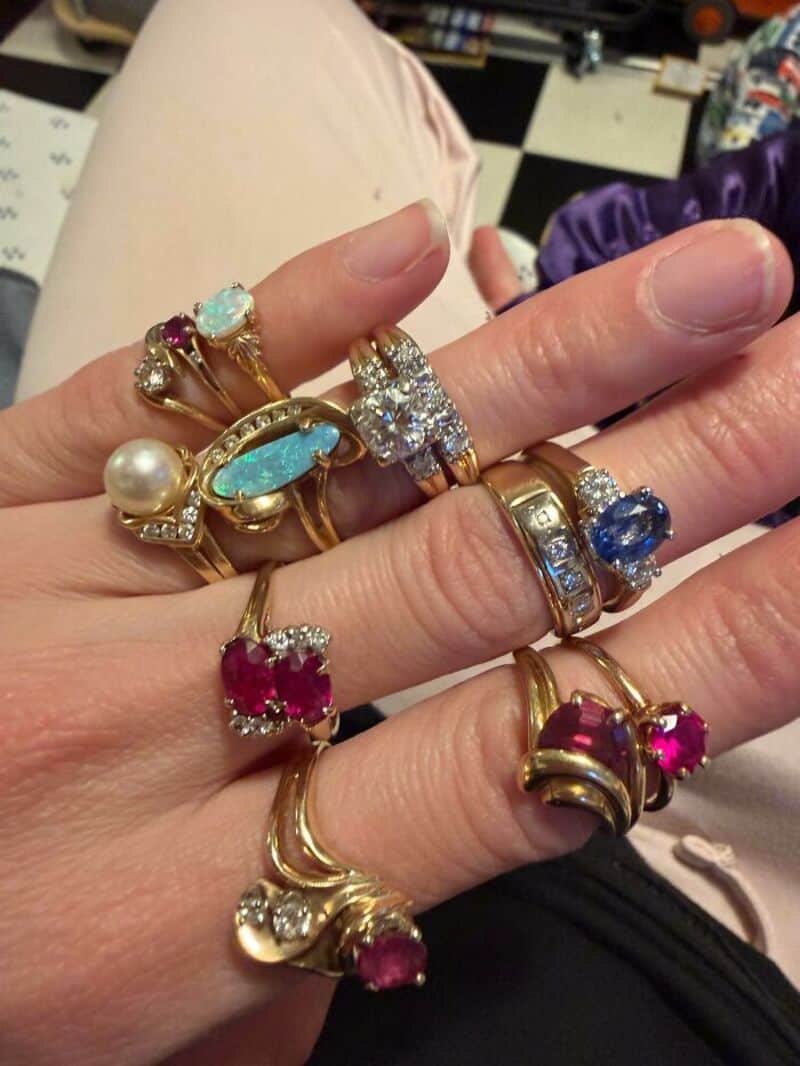 Multiple rings with colorful gemstones and pearls on a person's hand.