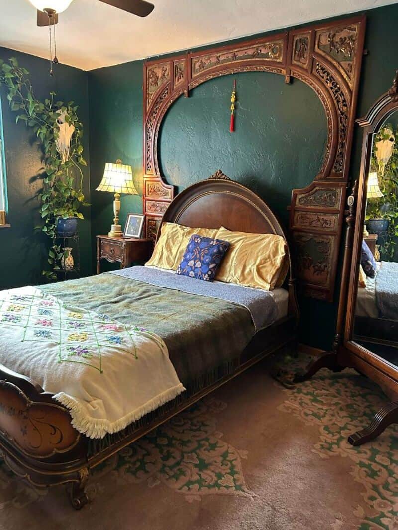 Vintage bedroom with ornate wooden headboard, green walls, and antique furniture.